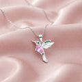 Collar colibrí plata 925 con zirconia rosada y esmeraldas sobre fondo rosa satinado