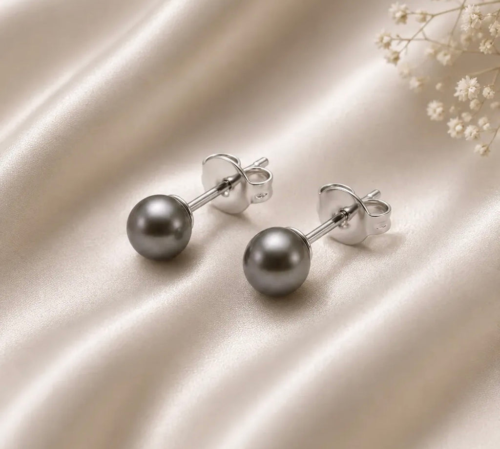 Detalle de aros de esfera gris con cierre de mariposa sobre tela satinada